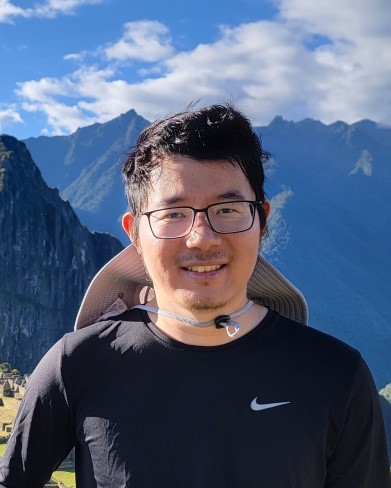 A person wearing glasses and a black shirt with mountains in the background  Description automatically generated